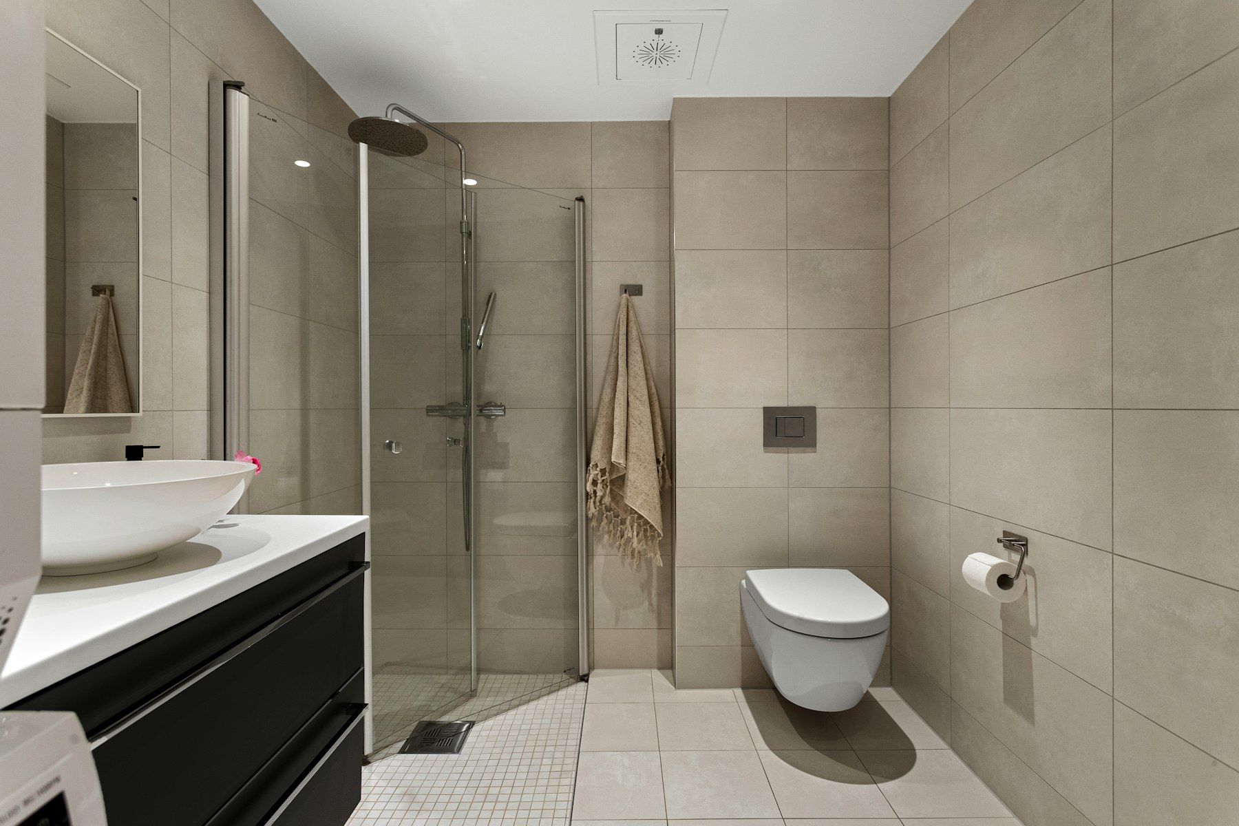 Bad mit beigen Wand- und Bodenfliesen, Glasdusche und wandhängendem WC