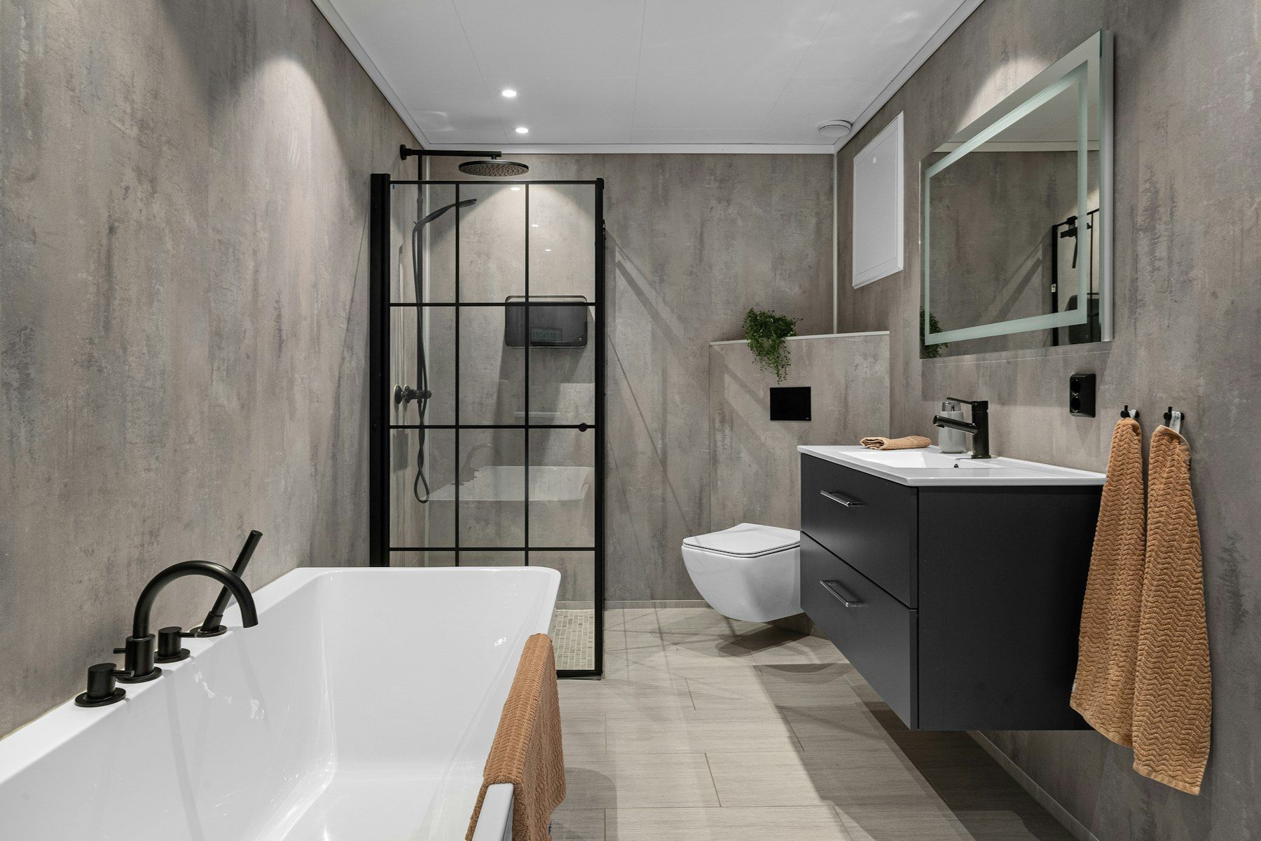 Saniertes Bad in Betonoptik mit freistehender Wanne, Dusche mit schwarzem Rahmen und wandhängendem WC