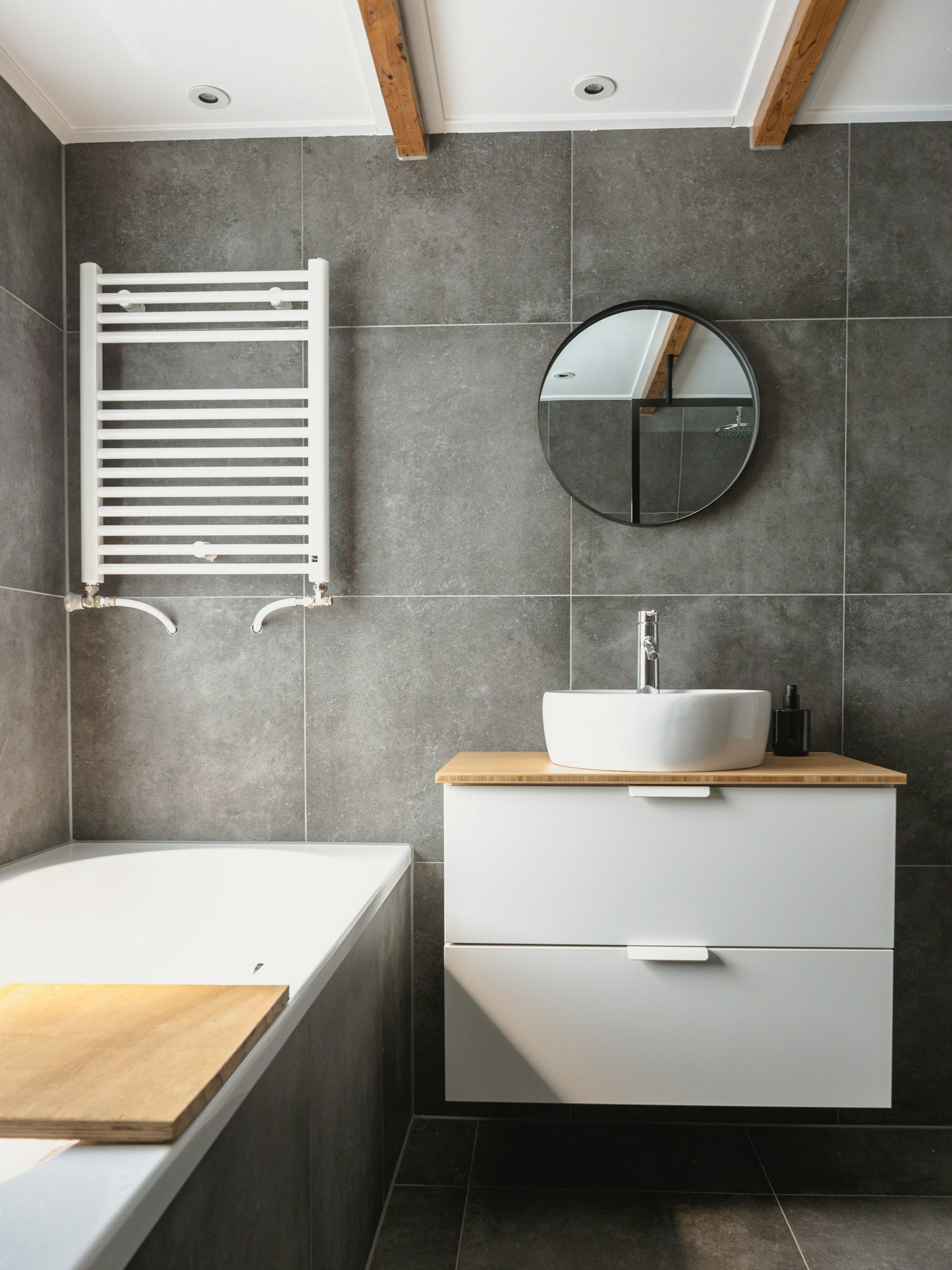 Bad mit großformatigen grauen Fliesen, Badewanne und Waschtisch mit Holzplatte