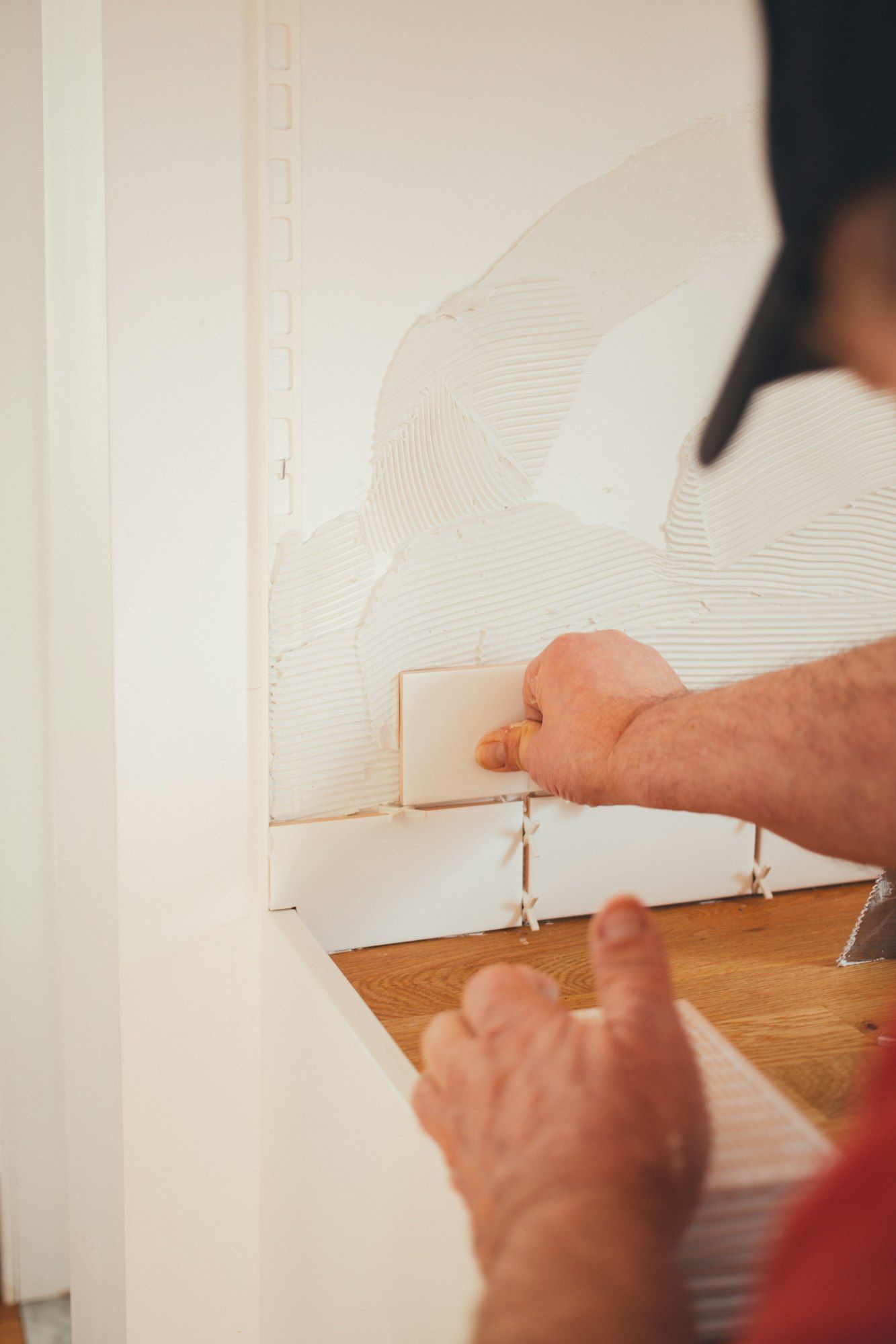 Fliesenleger setzt eine weiße Wandfliese mit Fliesenkreuzen ins Kleberbett