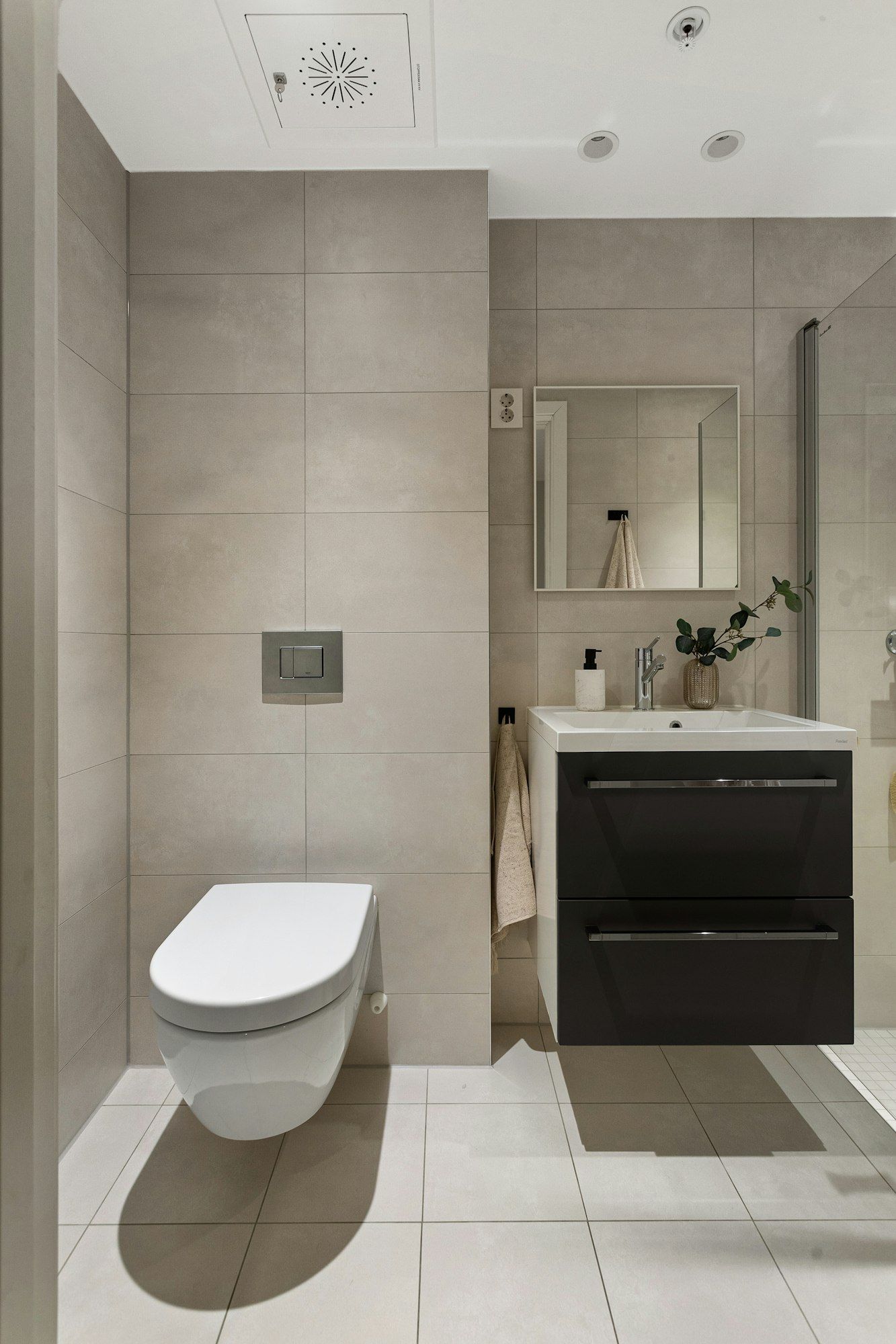 Kompaktes Gäste-WC mit großformatigen hellen Fliesen, wandhängendem WC und Waschtisch